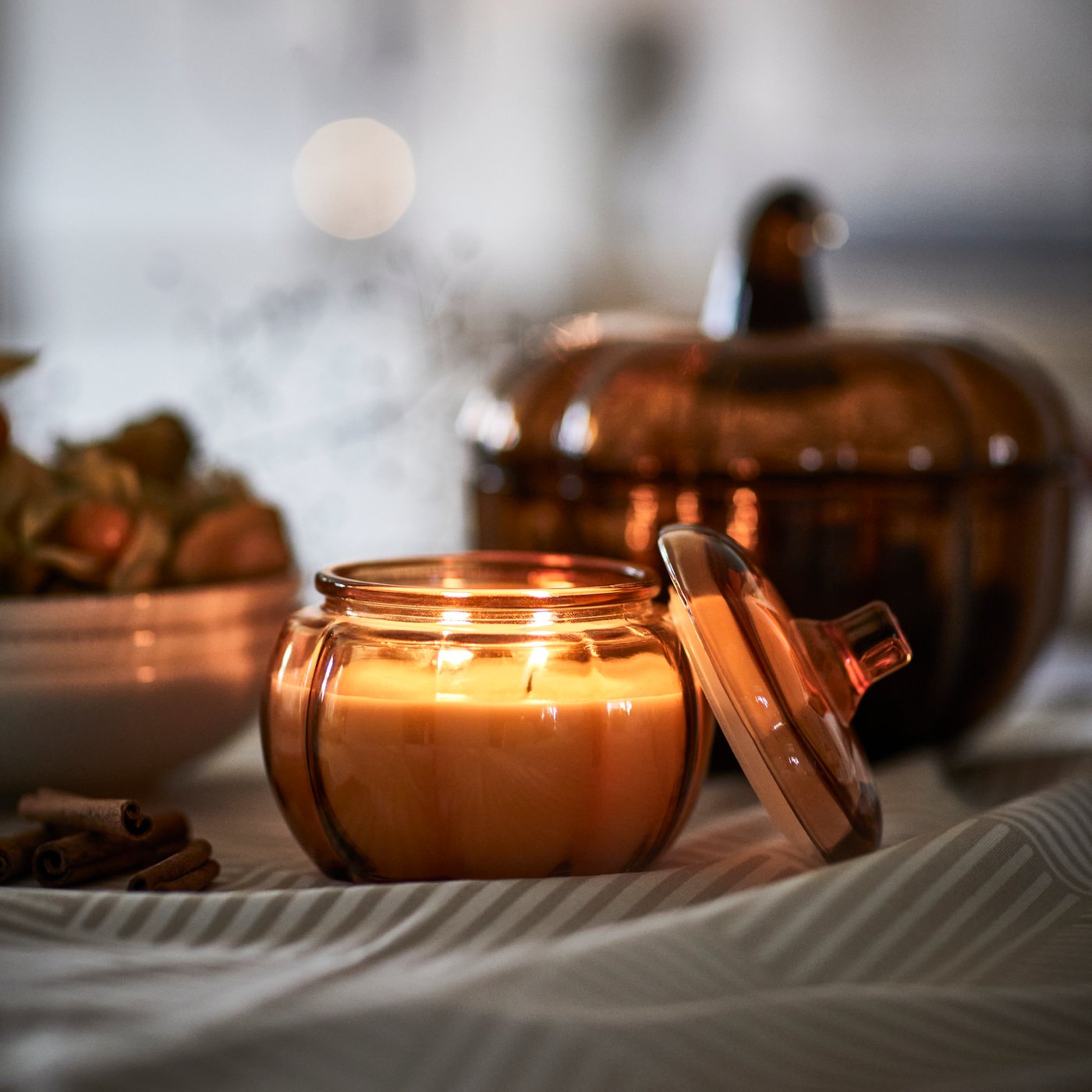vela perfumada num vidro decorado com abóboras acesa num ambiente escuro.