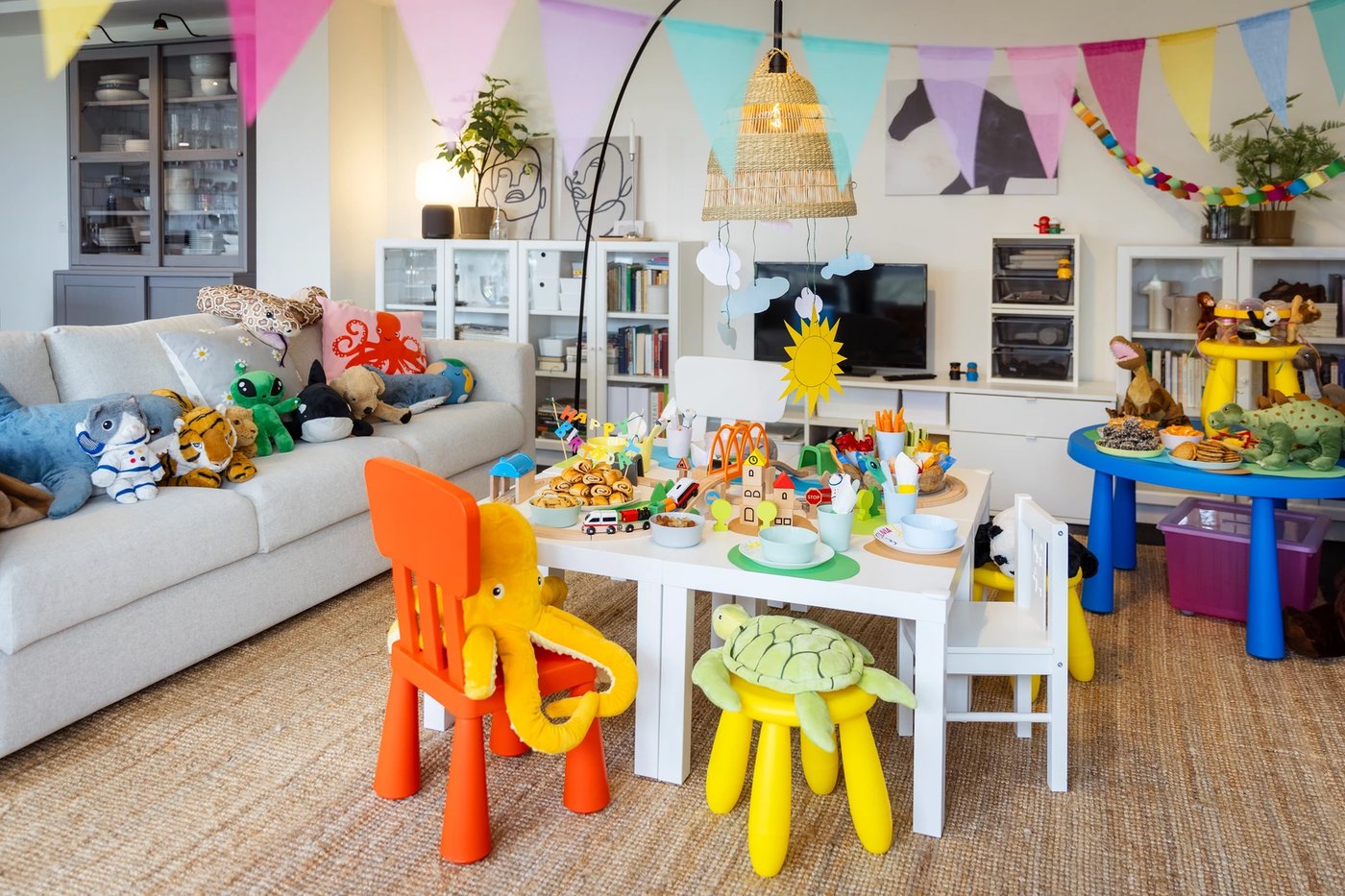 Blick auf den Geburtstagstisch. Viele Stofftiere sind eingeladen. Bunte niedrige Kinderstühle, auf dem Couchtisch wird das Essen in angenehmer Höhe serviert.