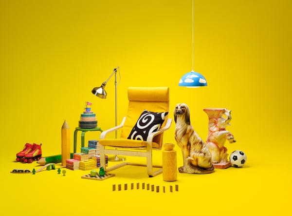 Image avec un fauteuil POÄNG Jaune et différents objets posés au sol à côté comme un chien en ceramique, un ballon de foot ...