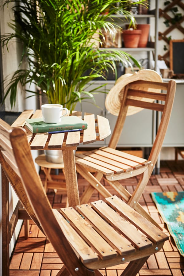 Silla plegable ASKHOLMEN junto a mesa ASKHOLMEN en una terraza con sol.