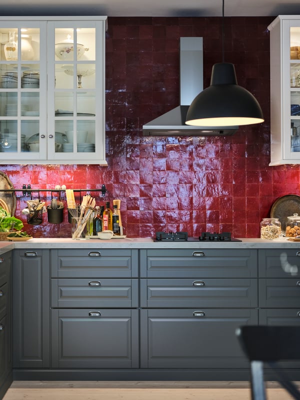 A neatly arranged, red-tiled kitchen with white wall cabinets, grey base cabinets and a white marble effect worktop.