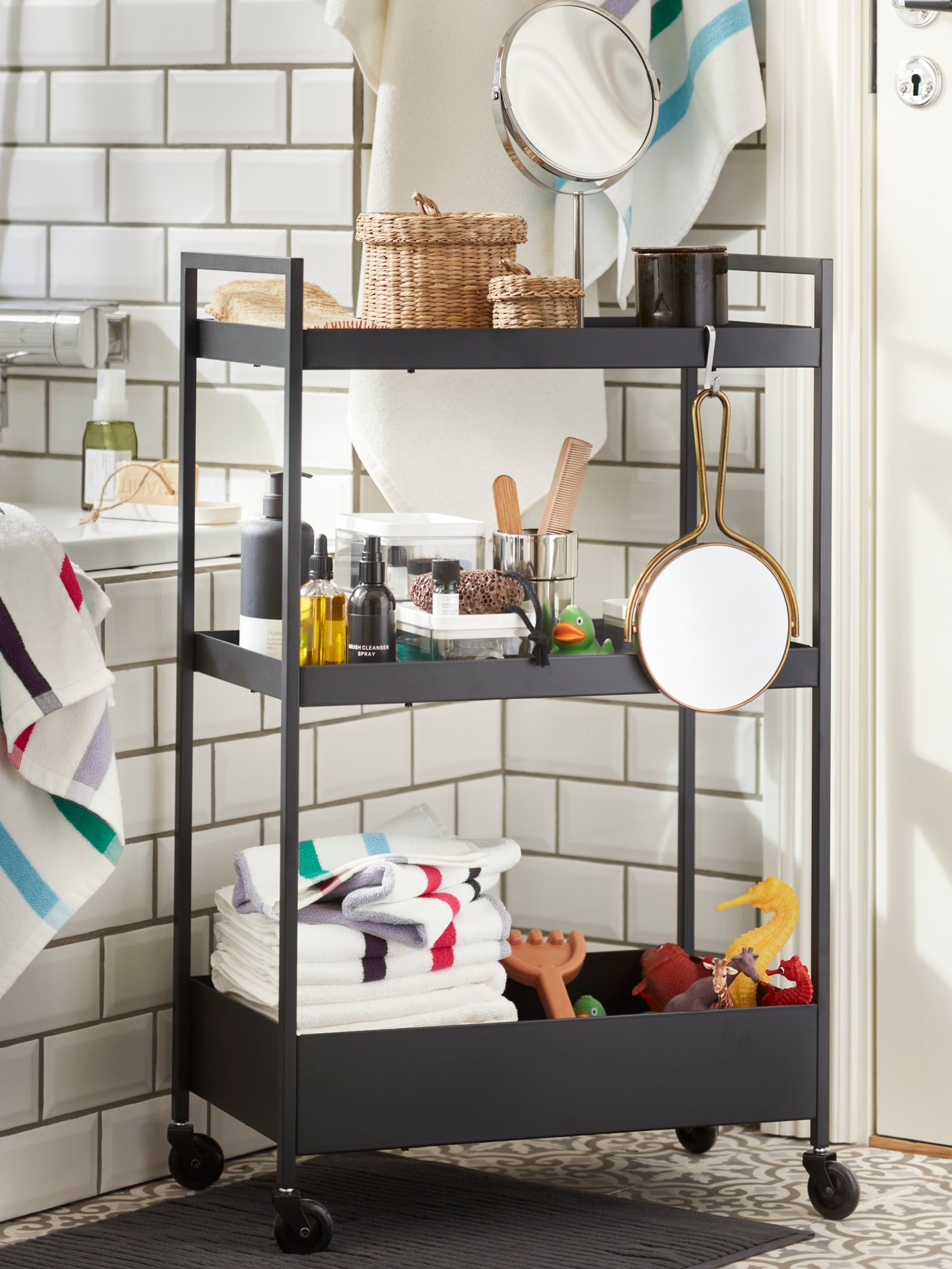 Zwart kastje op wielen in een badkamer met witte tegels.