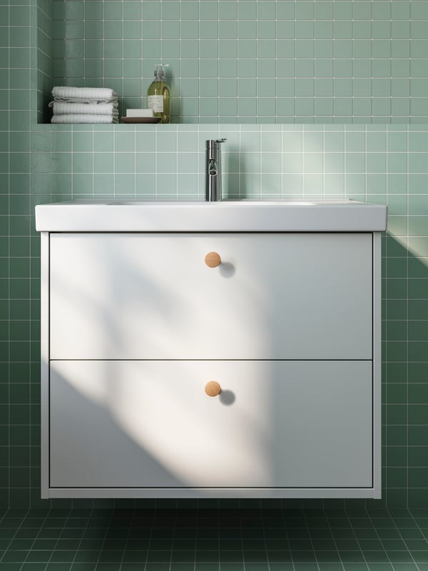 A white HAVBACK bathroom vanity with birch knobs hanging on a green tiled wall.