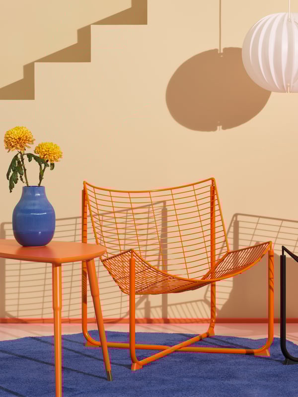 Es ist ein Raum in Weiß und Orange zu sehen. Hier gibt es ein orangefarbenes Kissen, einen orangefarbenen Stuhl und eine weiße Hängeleuchte.