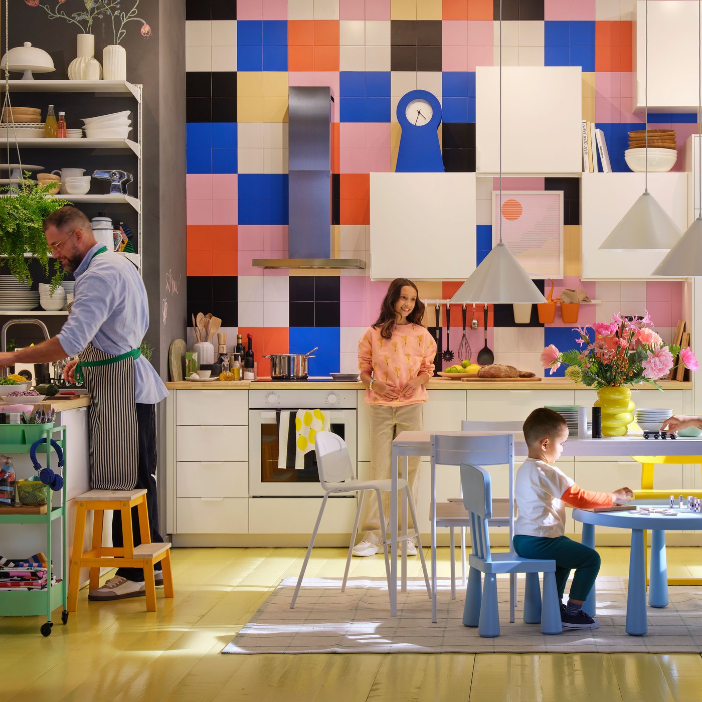 A family of three spending time together in a modern white kitchen with a high ceiling and large, brightly covered tiles.