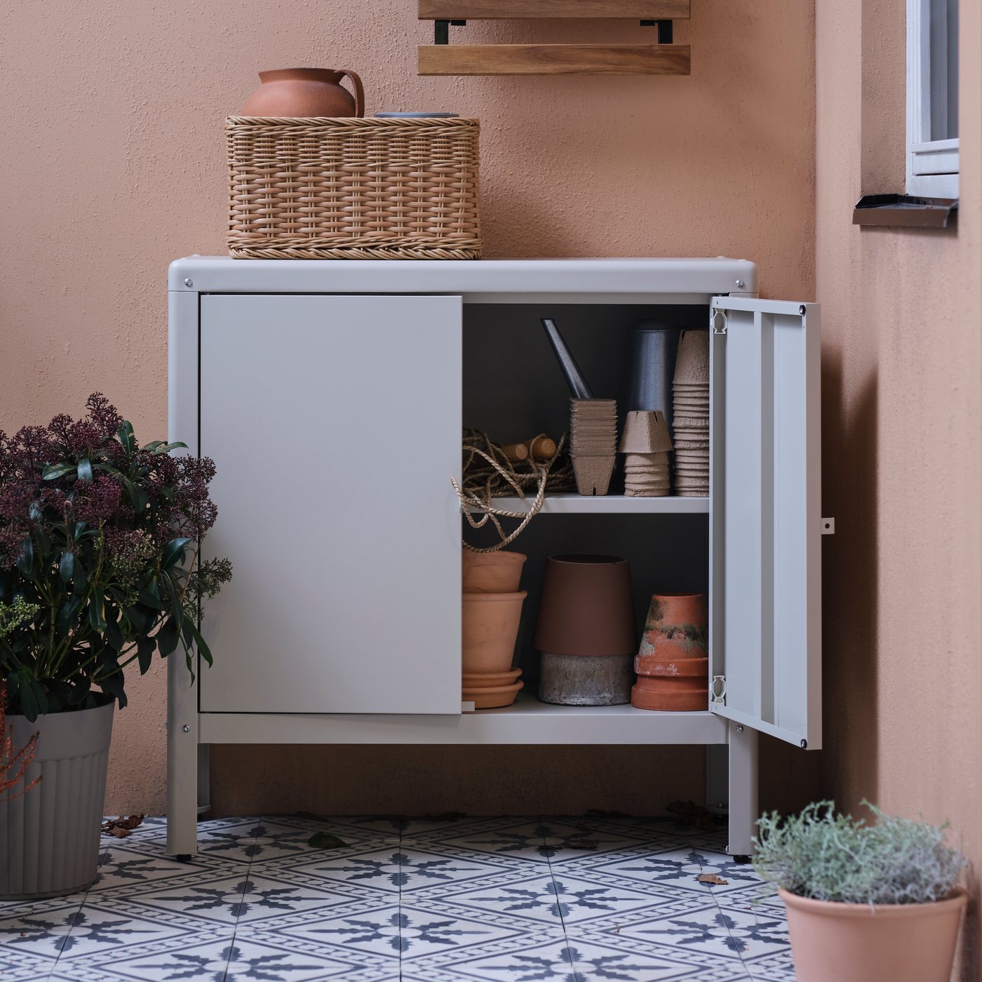 A KOLBJÖRN cabinet holding many items, including MUSKOTBLOMMA plant pots with saucers, stands on a balcony.