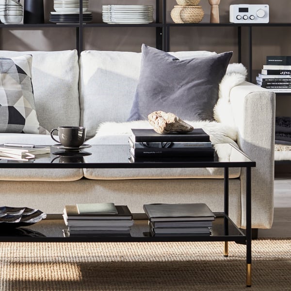 Une table basse en verre noir au milieu d’un salon où sont posés divers accessoires. 