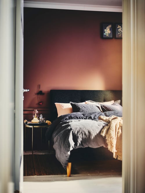 Bedroom area featuring a grey, upholstered bed frame with a duvet set and pillows, and a tray table with a table lamp.