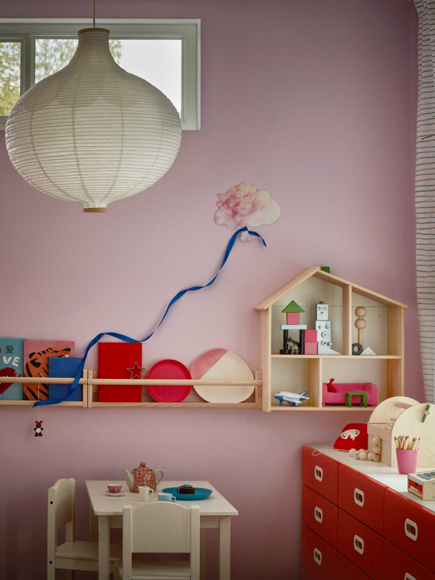 Dormitorio infantil con casa de muñecas, mesa infantil, cómoda, silla infantil, almacenaje de pared y pantalla para lámpara de techo.