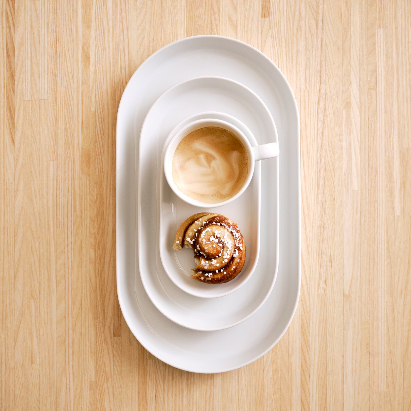Mehrere Größen der weißen IKEA 365+ Servierplatte mit einer angebissenen Zimtschnecke und einem Kaffee darauf.