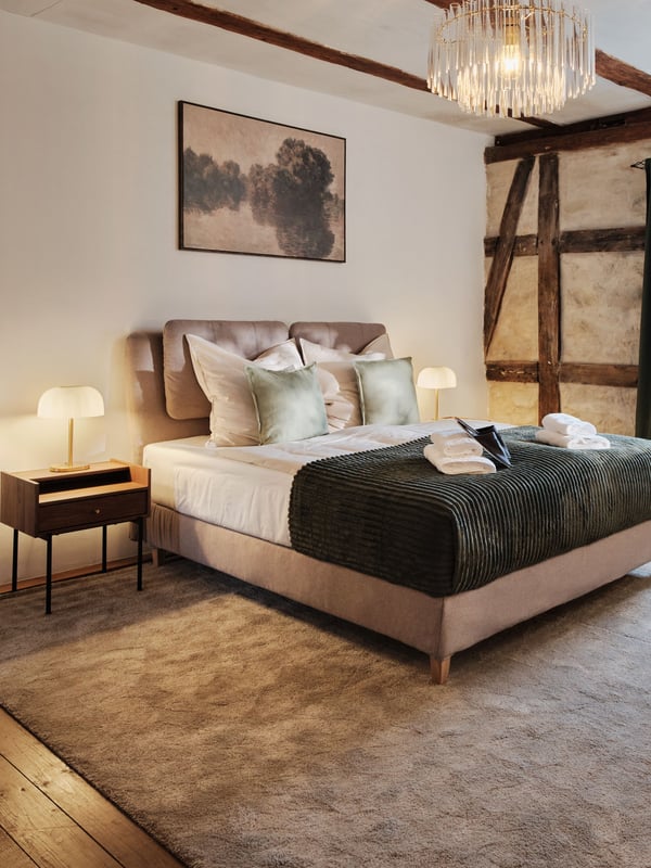 Hotelzimmer mit Bett und grünem Überwurf