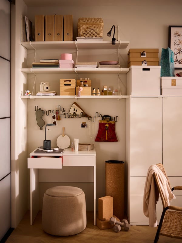 A white BRIMNES dressing table with white BERGSHULT/PERSHULT wall shelves above and a dark-beige JÄRRESTAD pouffe beneath.