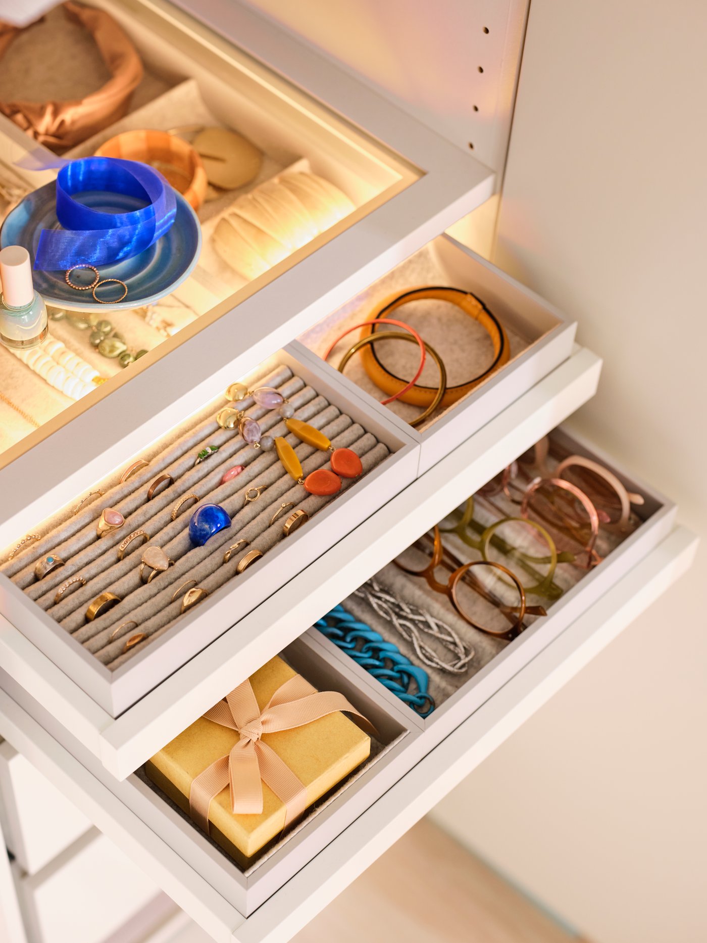 Close-up of KOMPLEMENT glass shelf with inserts for pull-out trays below, with jewelry and accessories in neat order.