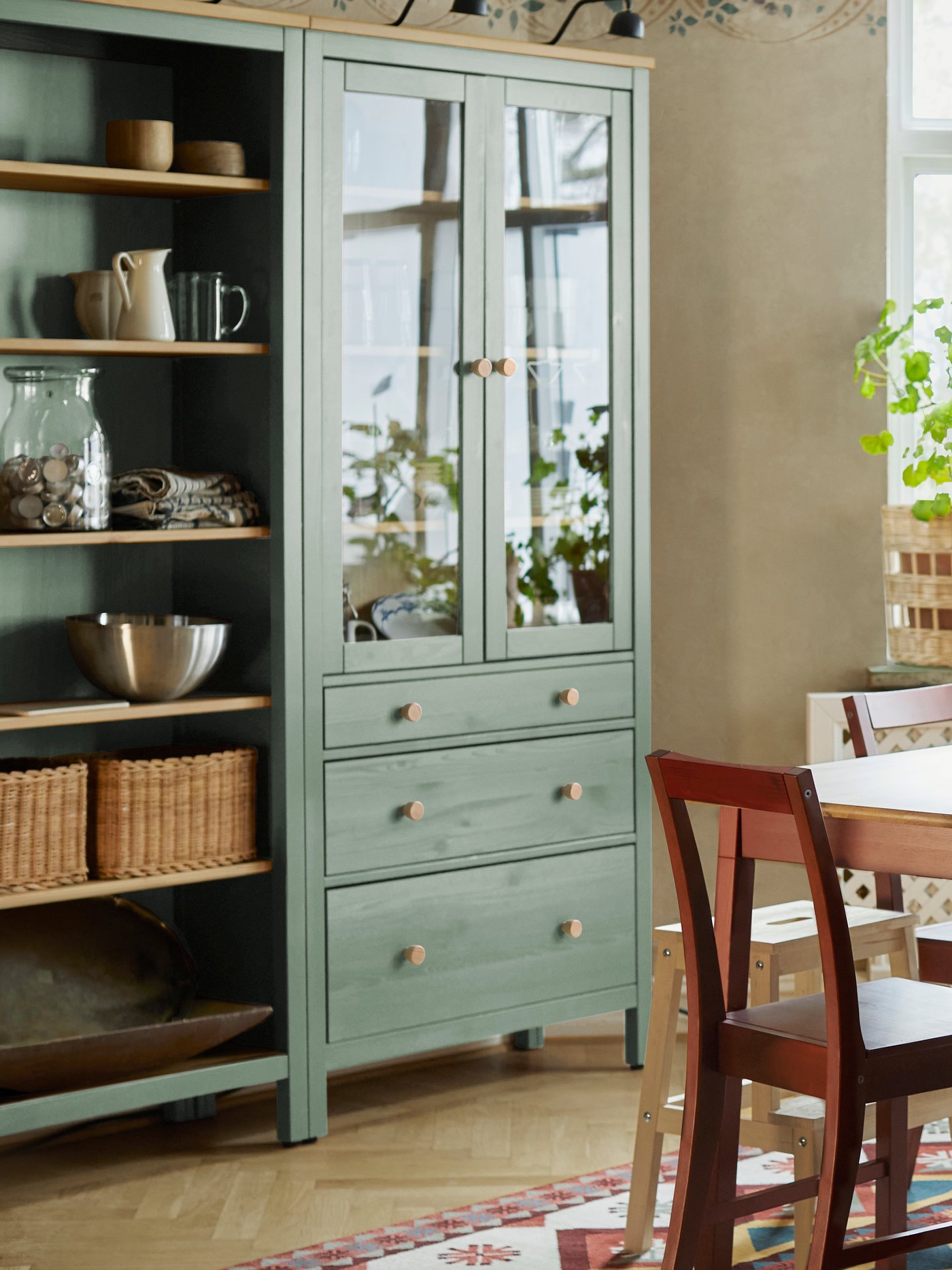 Una combinazione mobili HEMNES grigio-verde/mordente marrone chiaro con cassetti e due ante di vetro posto in una cucina.