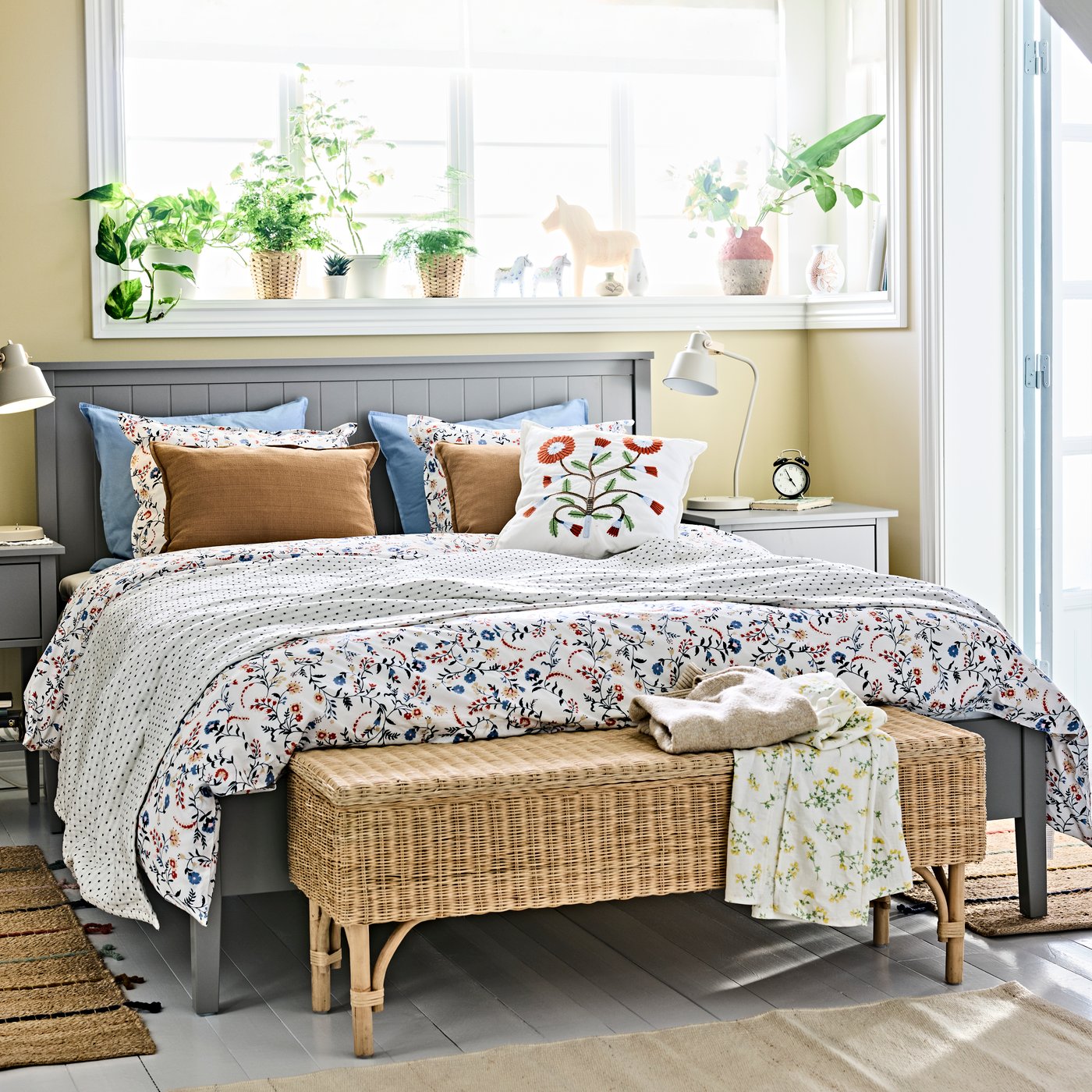 A bedroom setup featuring a neatly made bed with patterned textiles, bedside tables on each side and a woven bench in front.
