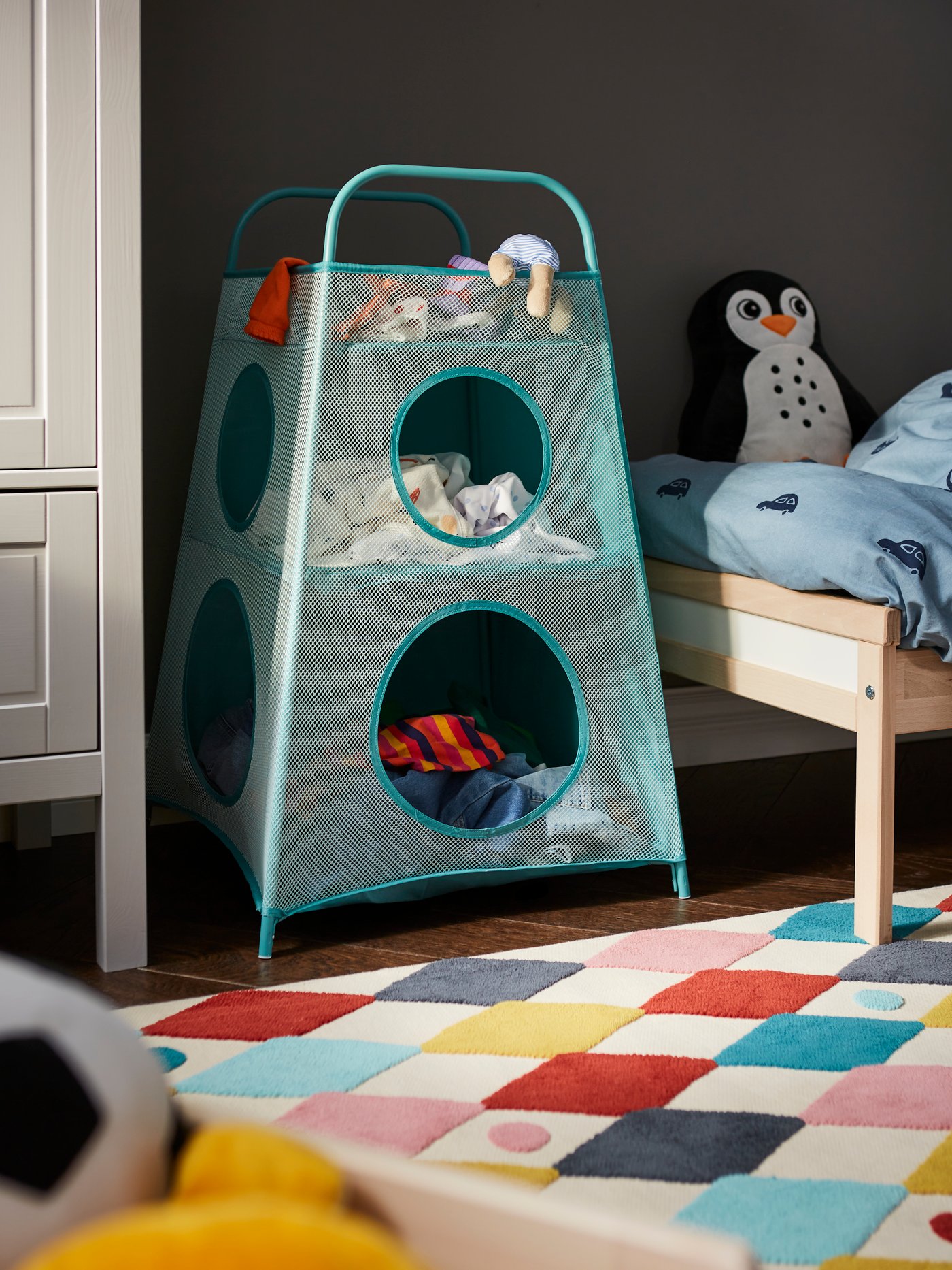 Una habitación infantil con una estantería TIGERFINK turquesa con compartimentos colocada junto a una alfombra BUSENKEL rectangular.