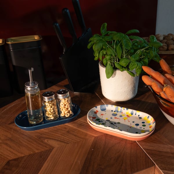 Dettaglio di un piano di lavoro in legno con un set di contenitori per olio e spezie, una piantina di basilico e due piccoli piatti ovali decorati.