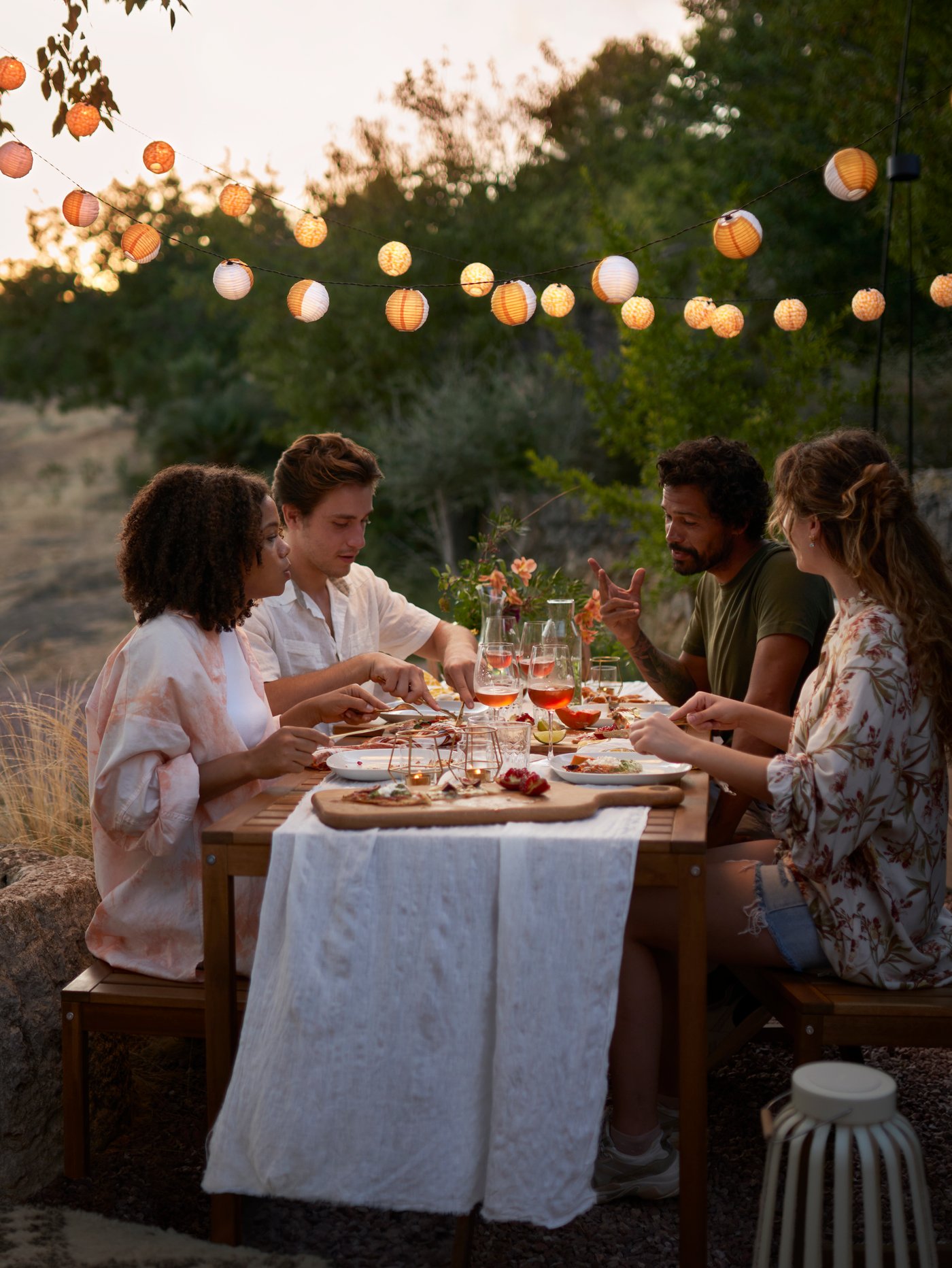 Fyra personer sitter och äter och pratar runt ett bord i en trädgård.