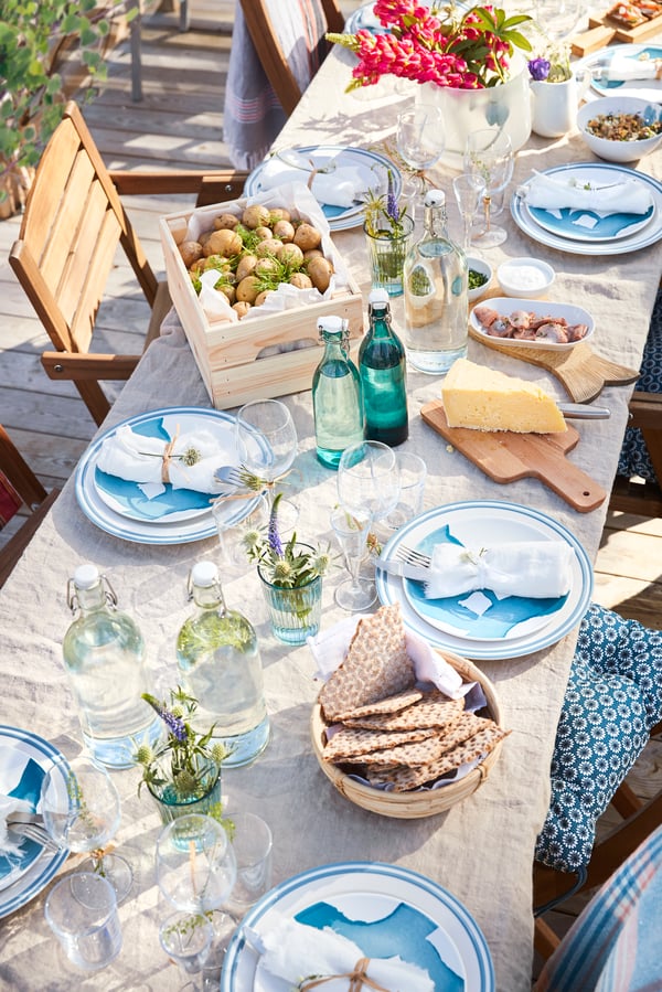 A close up of an outdoor dining table with dinnerware, glasswar, food and drink.