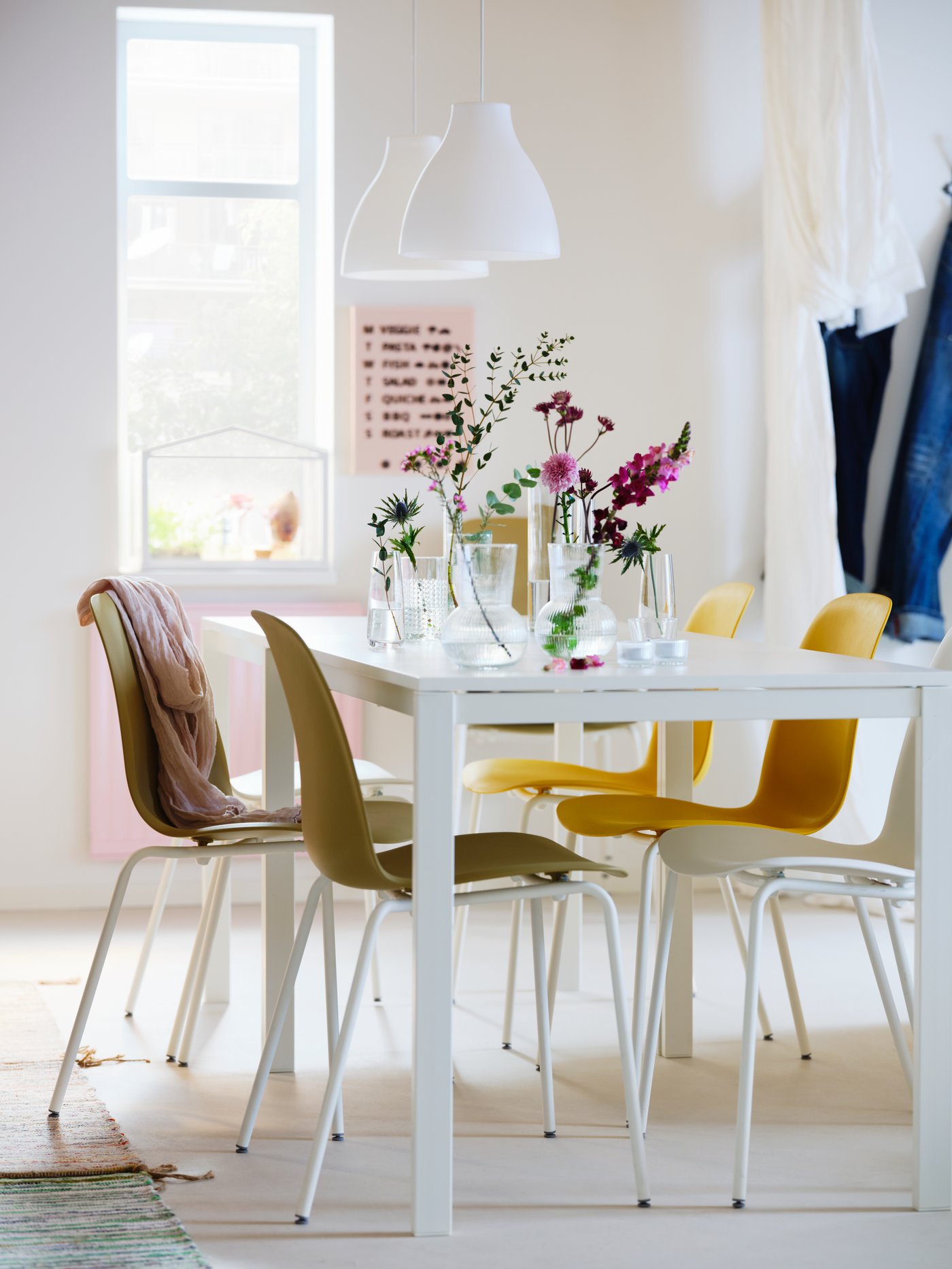 A dining area in white shades with two white MELLTORP tables, white MELODI pendants and different-colour LEIFARNE chairs.