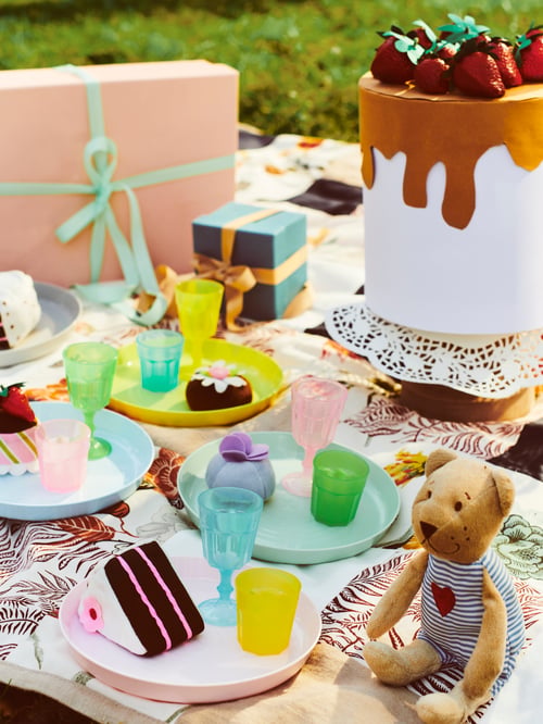 Leuchtend buntes Kinderpicknick mit bunten DUKTIG Gläsern, KALAS Tellern in verschiedenen Farben und FABLER BJÖRN Stofftier.