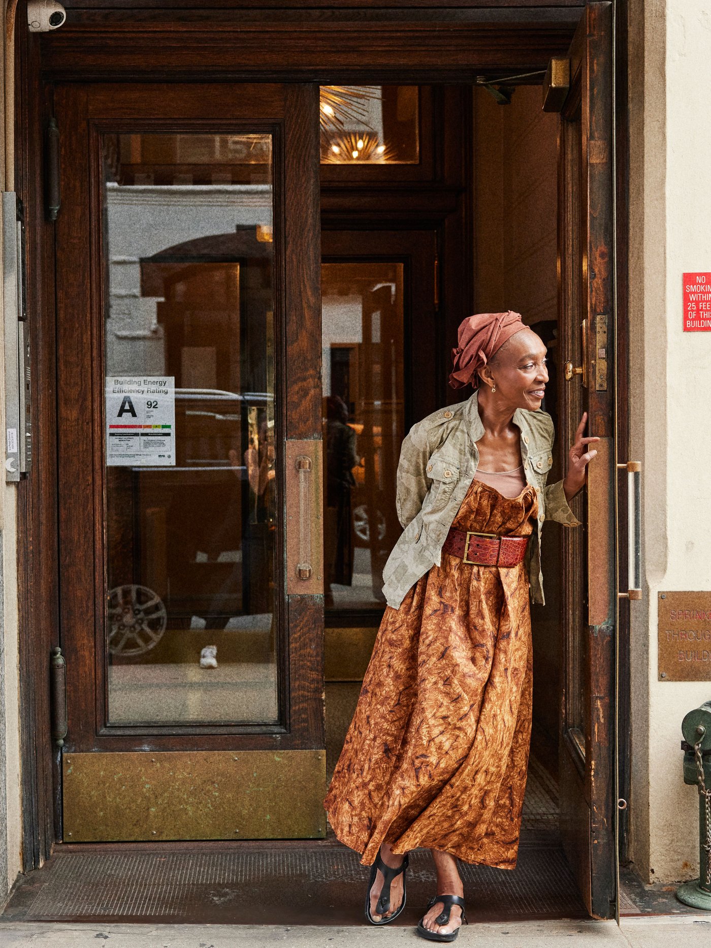 A woman stands outside her home and leans against the door in profile.