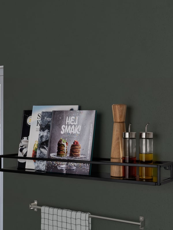 Una repisa LINDÅSEN en la pared de una cocina. En su interior contiene un salero, aceiteros y algunos libros de cocina.