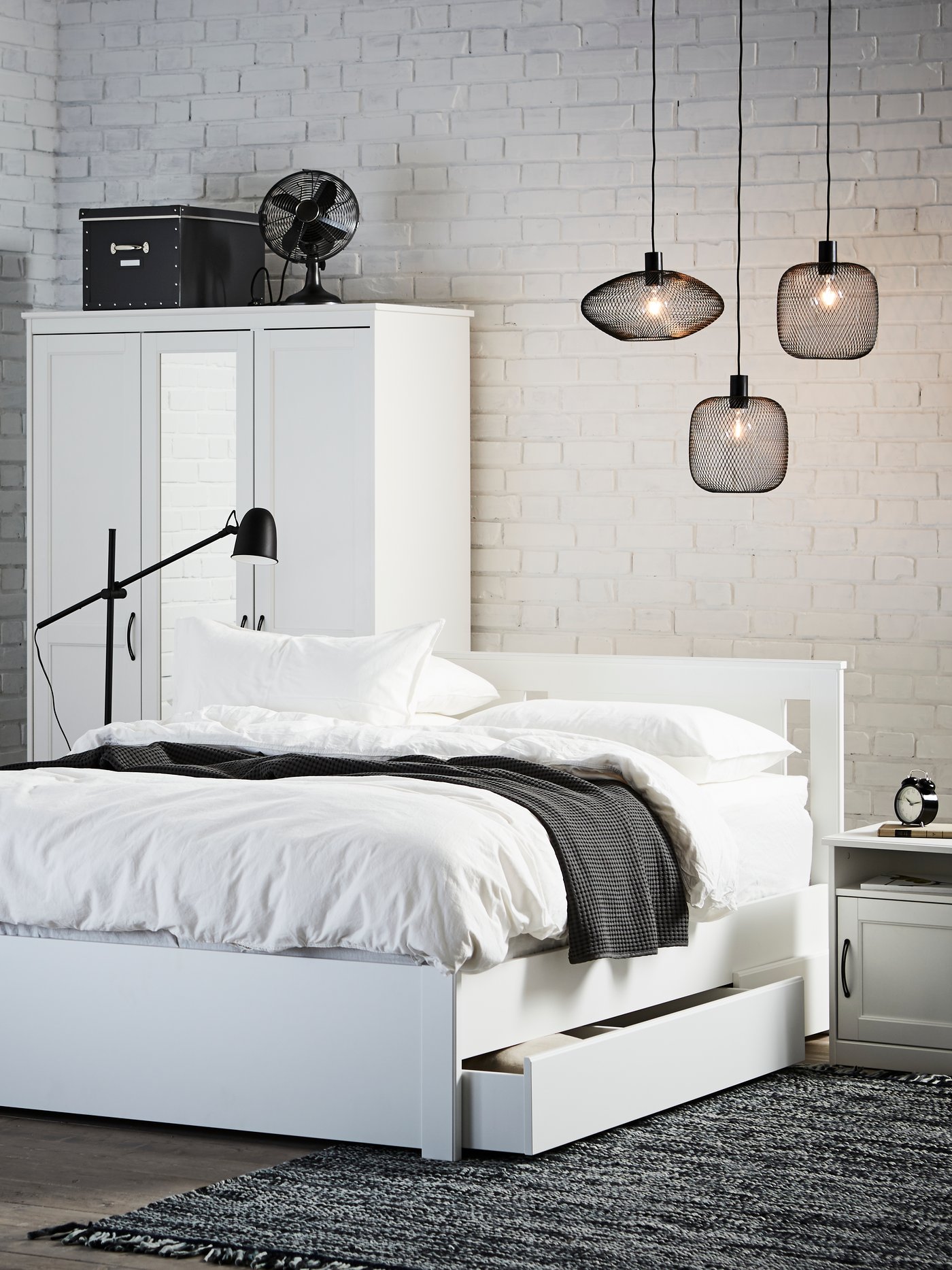 Una lampada da terra/da lettura SKURUP nera in camera da letto con un letto bianco e tre lampade sospese da soffitto.