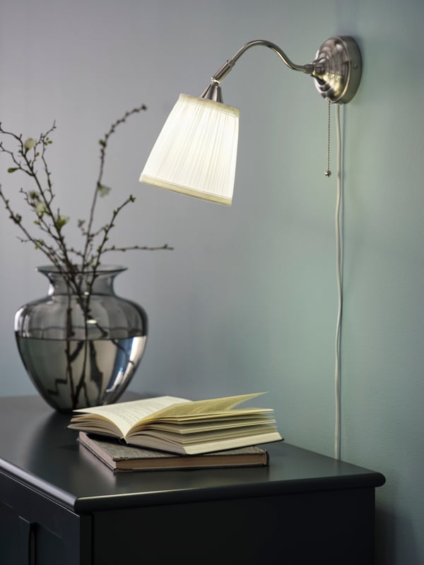 IKEA ÅRSTID nickel-plated/white wall lamp on top of a sideboard in the hallway.