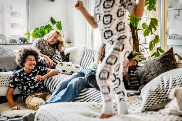 Fire børn leger og sidder i en sofa, en kvinde sidder i hjørnet af sofaen og griner.