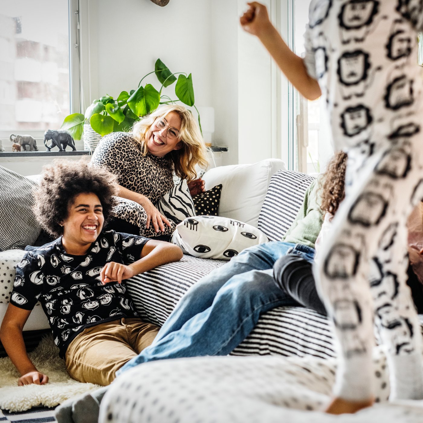 Fire børn leger og sidder i en sofa, en kvinde sidder i hjørnet af sofaen og griner.