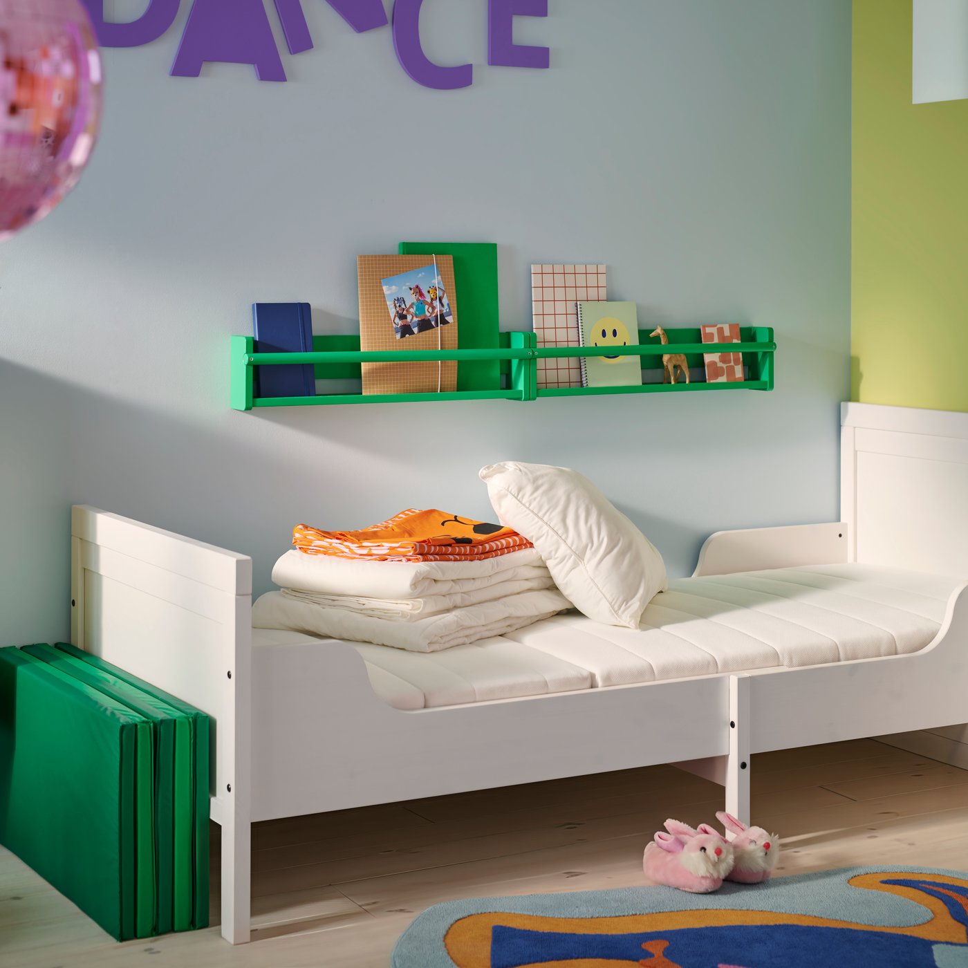 A white BUSUNGE extendable bed with a VIMSIG foam extendable mattress in a blue children’s room with folded textiles on top.