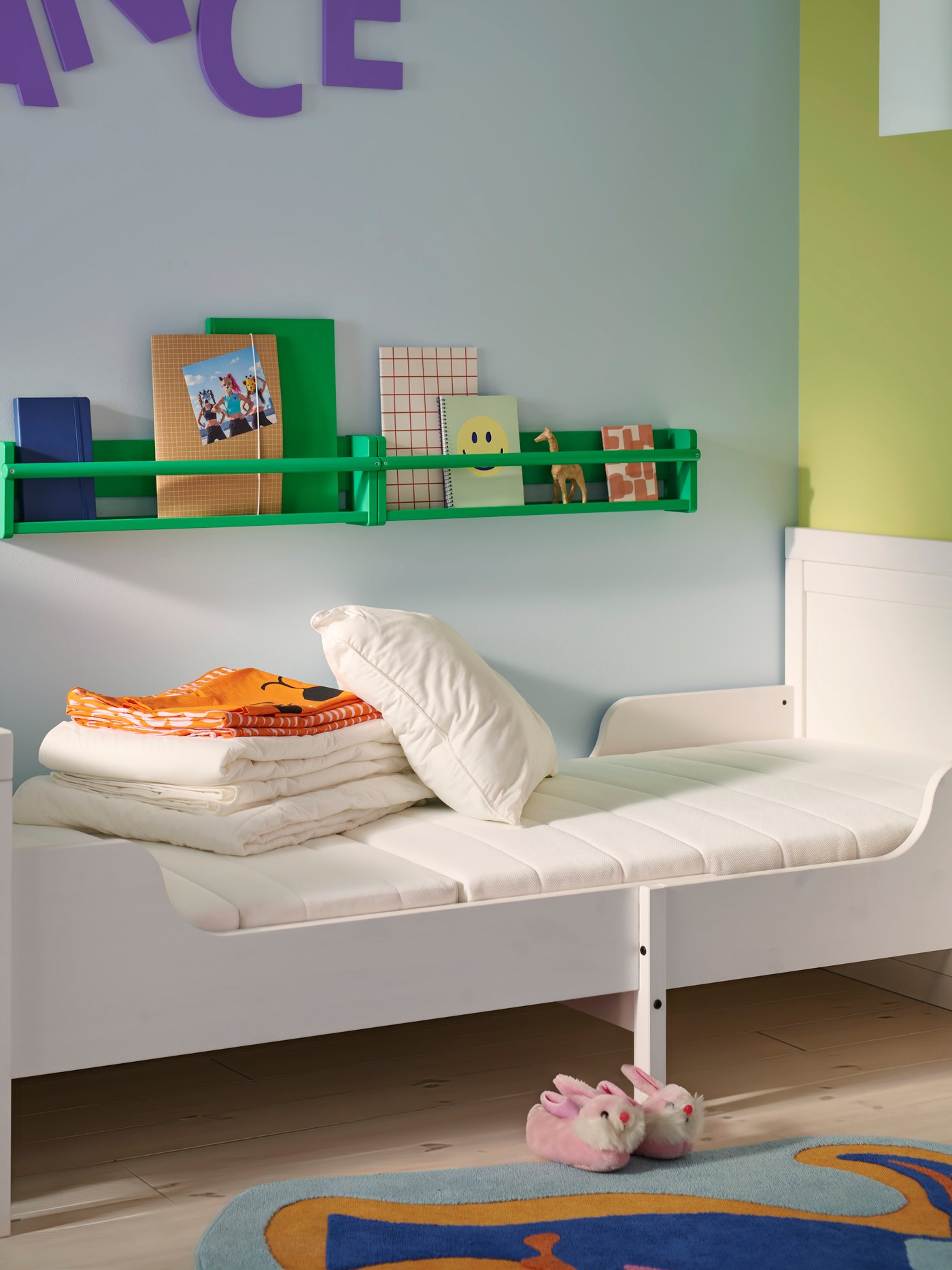 A white BUSUNGE extendable bed with a VIMSIG foam extendable mattress in a blue children’s room with folded textiles on top.