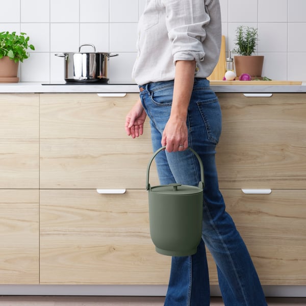 Person carrying a waste bin in the kitchen