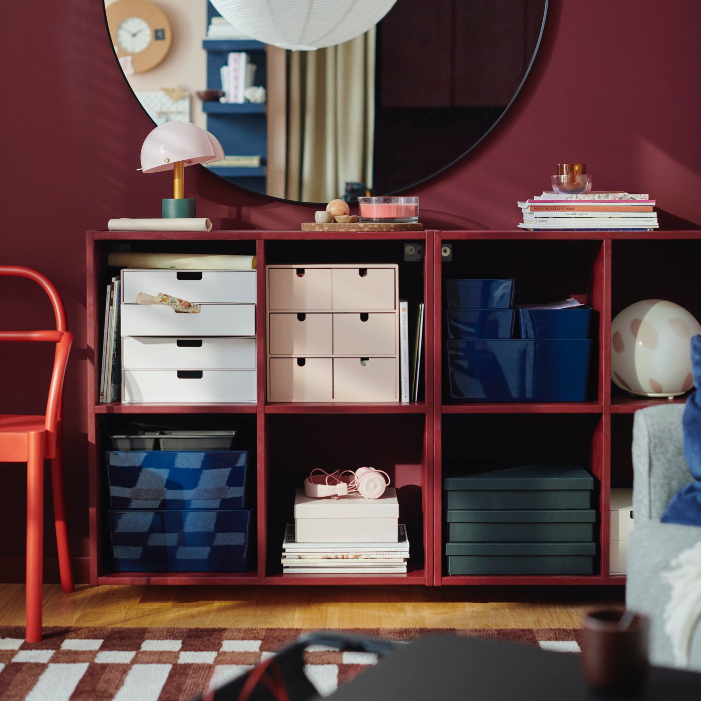 Two IVAR shelving units, painted red, containing a MOPPE mini chest of drawers and FJÄDERHARV storage boxes.