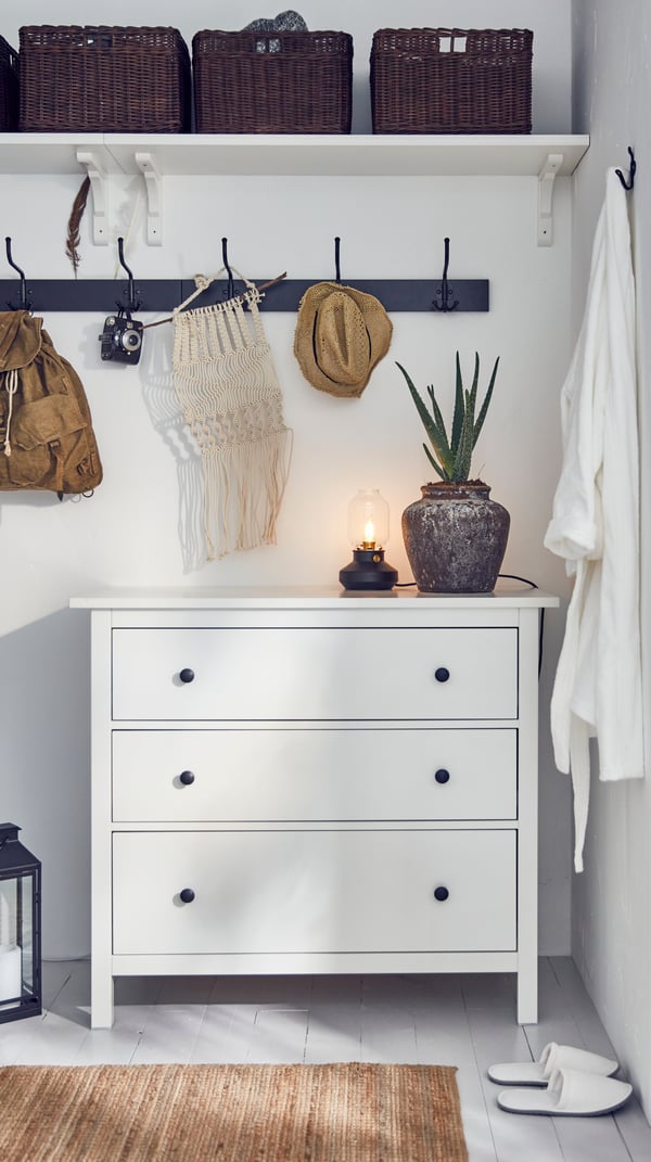 Biała komoda IKEA HEMNES z 3 szufladami w sypialni, a nad nią drążek i półka z koszykami.