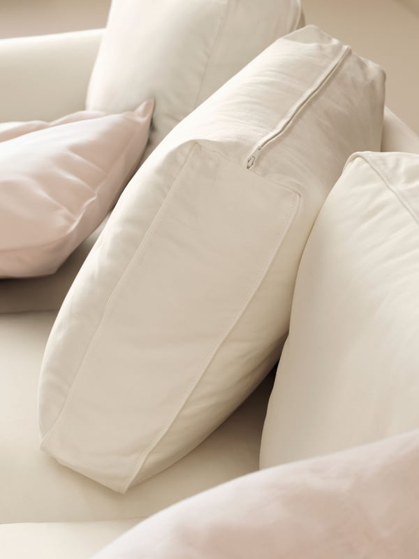 Ryggputene til en EKTORP sofa med beige trekk. Den ene puta er plassert på skrå, og det ligger også noen ekstra puter på setet.