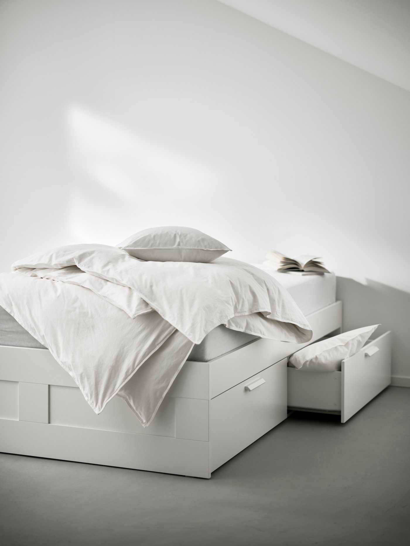 Una daybed IKEA con marco blanco y dos cajones. Uno de ellos abierto con un plumón adentro.