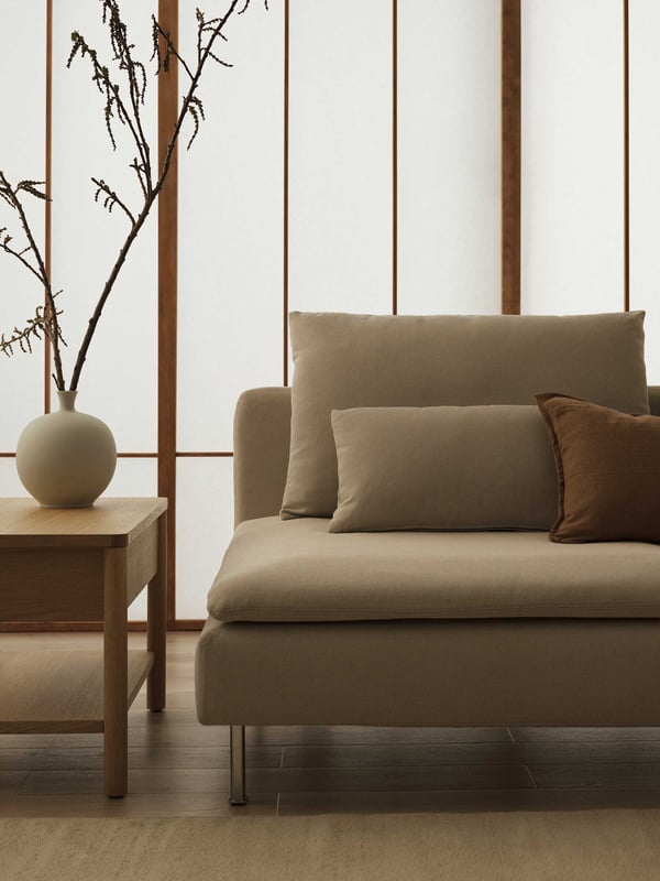 Minimalistiskt vardagsrum i japandi-stil med beige SÖDERHAMN soffa, två kuddar, träbord och rund vas med grenar. Bakgrund med träinramade, halvgenomskinliga paneler.

