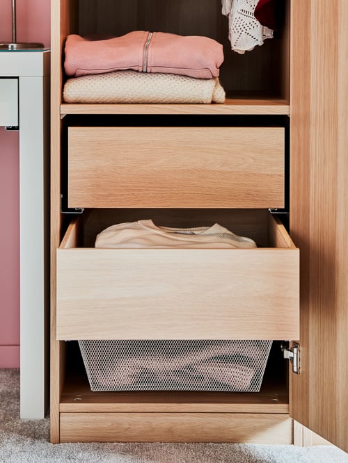A close-up of the bottom of a slim wardrobe's interior with two white stained oak effect KOMPLEMENT drawers holding clothes.