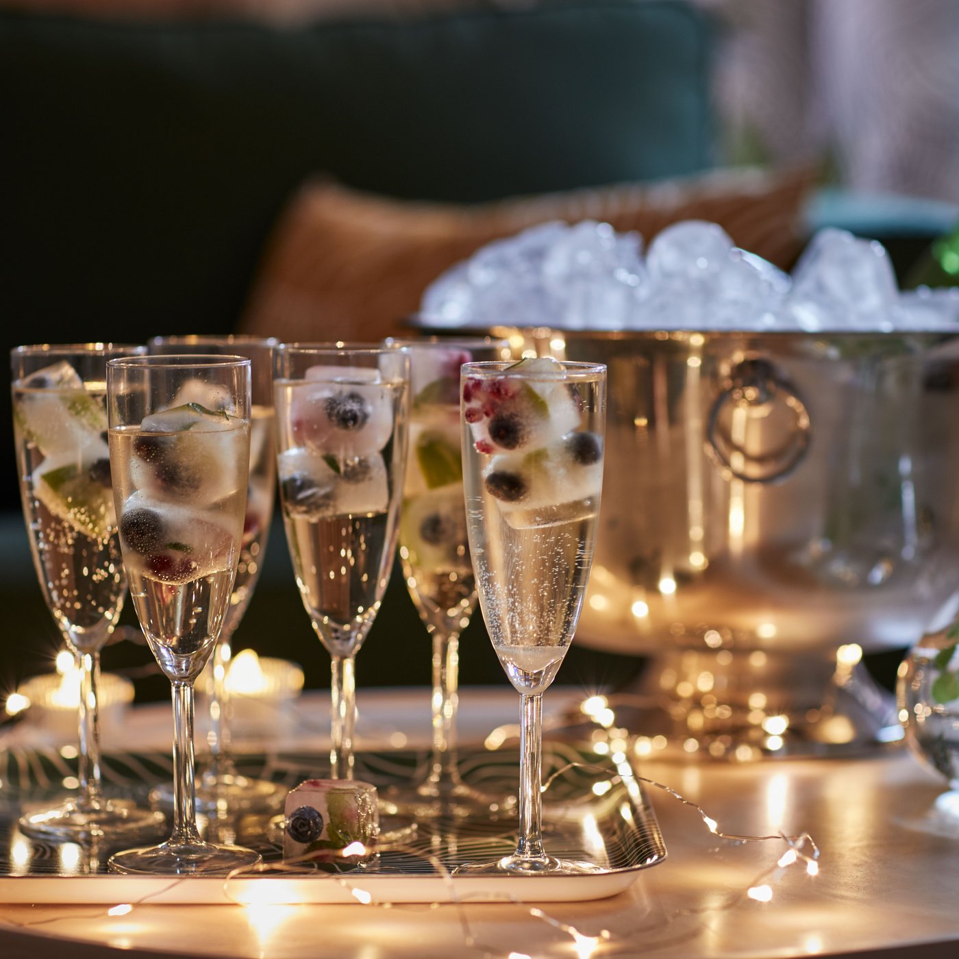 Mehrere SVALKA Sektgläser gefüllt mit Eiswürfeln und einem Getränk stehen auf einem silbernen Tablett und dahinter steht ein großes Gefäß mit vielen Eiswürfeln