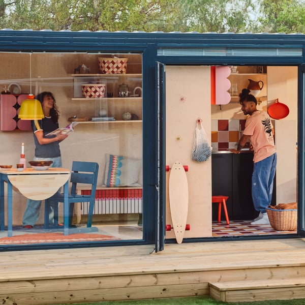 Una piccola casa su una pedana, con pareti e porte in vetro, vista dall'esterno. All'interno ci sono mobili e decorazioni OMMJÄNGE.