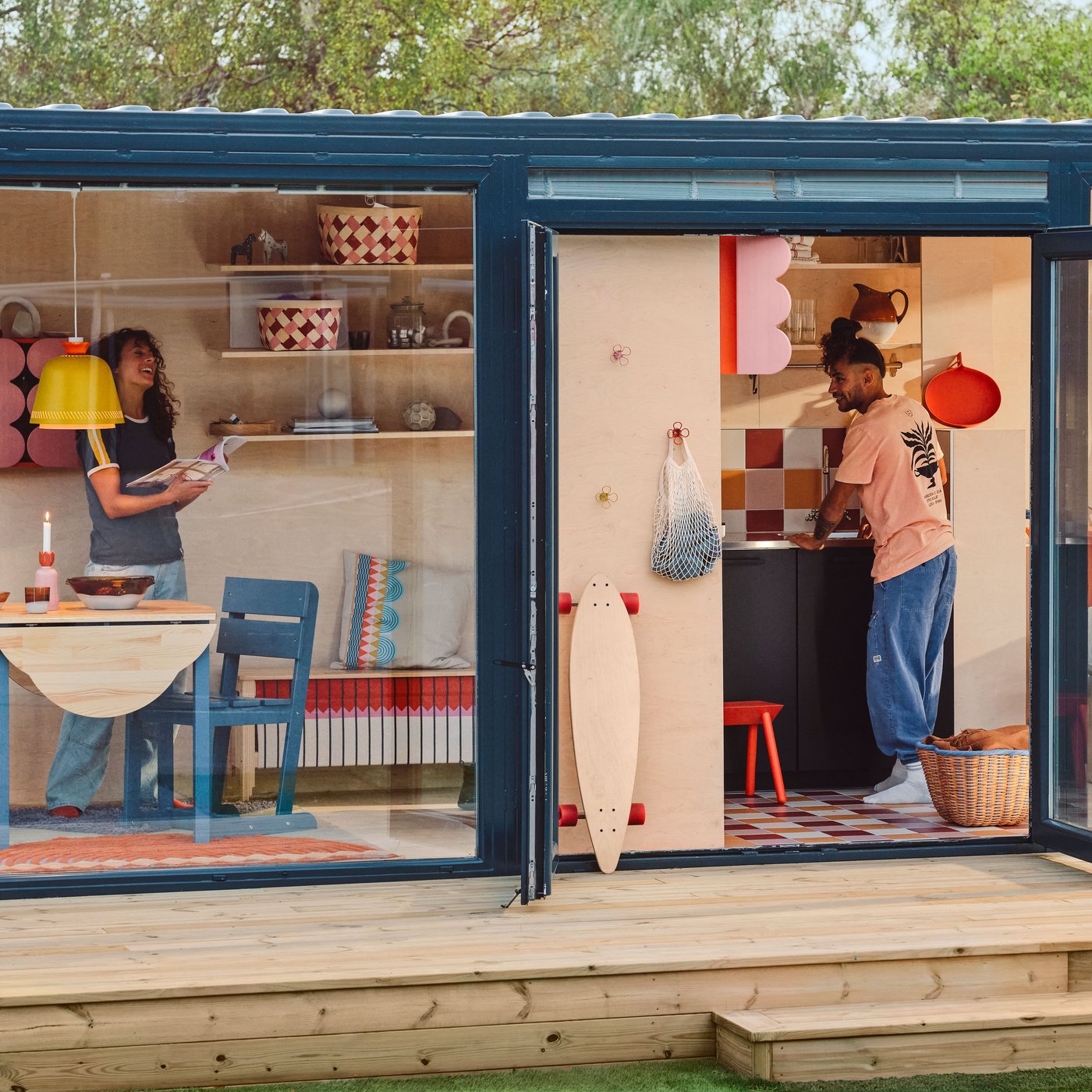 A tiny house on a deck, with glass walls and doors, seen from outside. There are OMMJÄNGE furnishings and decorations inside.