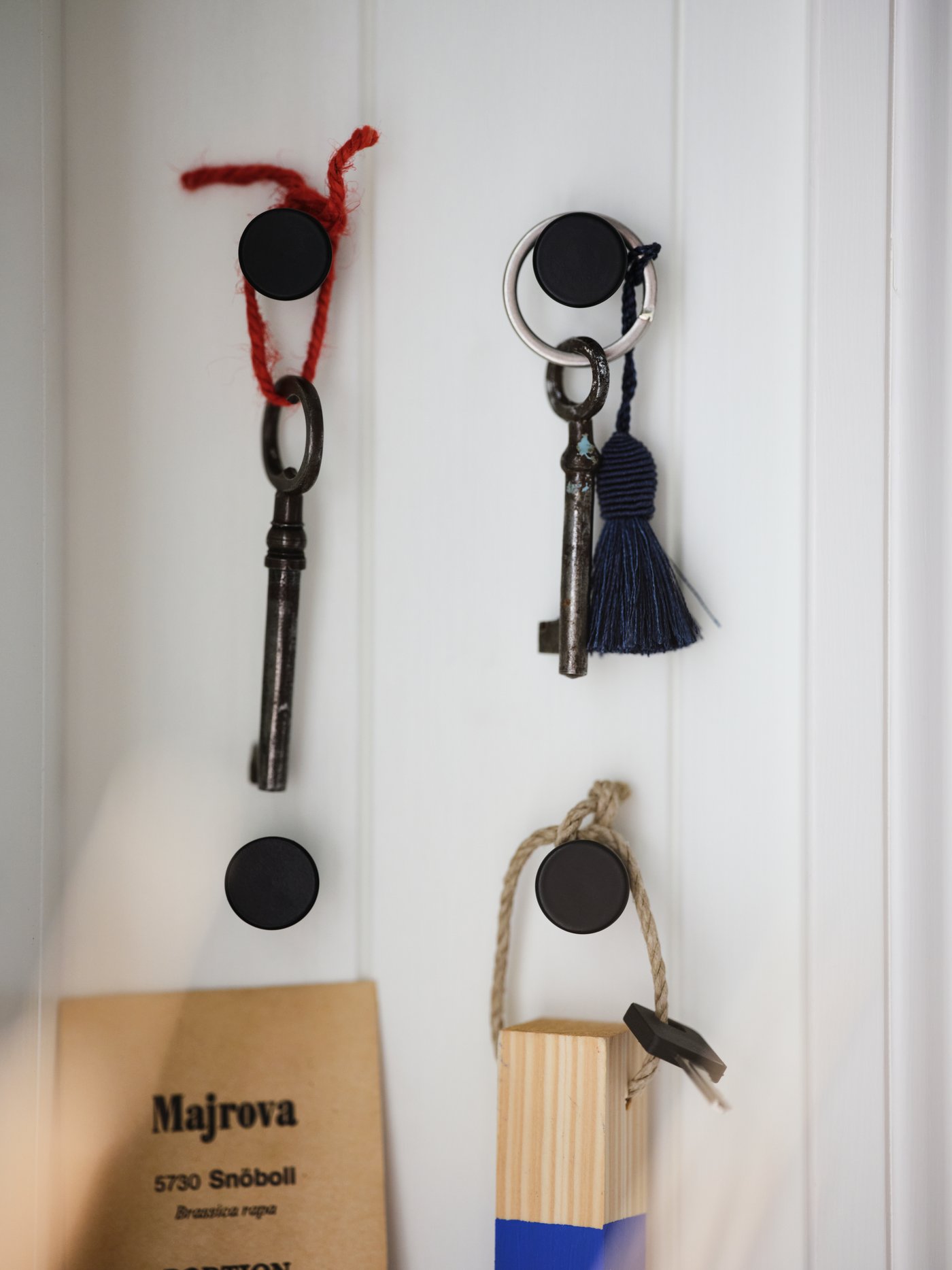 Schlüssel und Accessoires an vier schwarzen SKOGSVIKEN Haken, deren Platzierung ein Rechteck bildet. Die Haken sind an einer weiss getäfelten Wand befestigt.