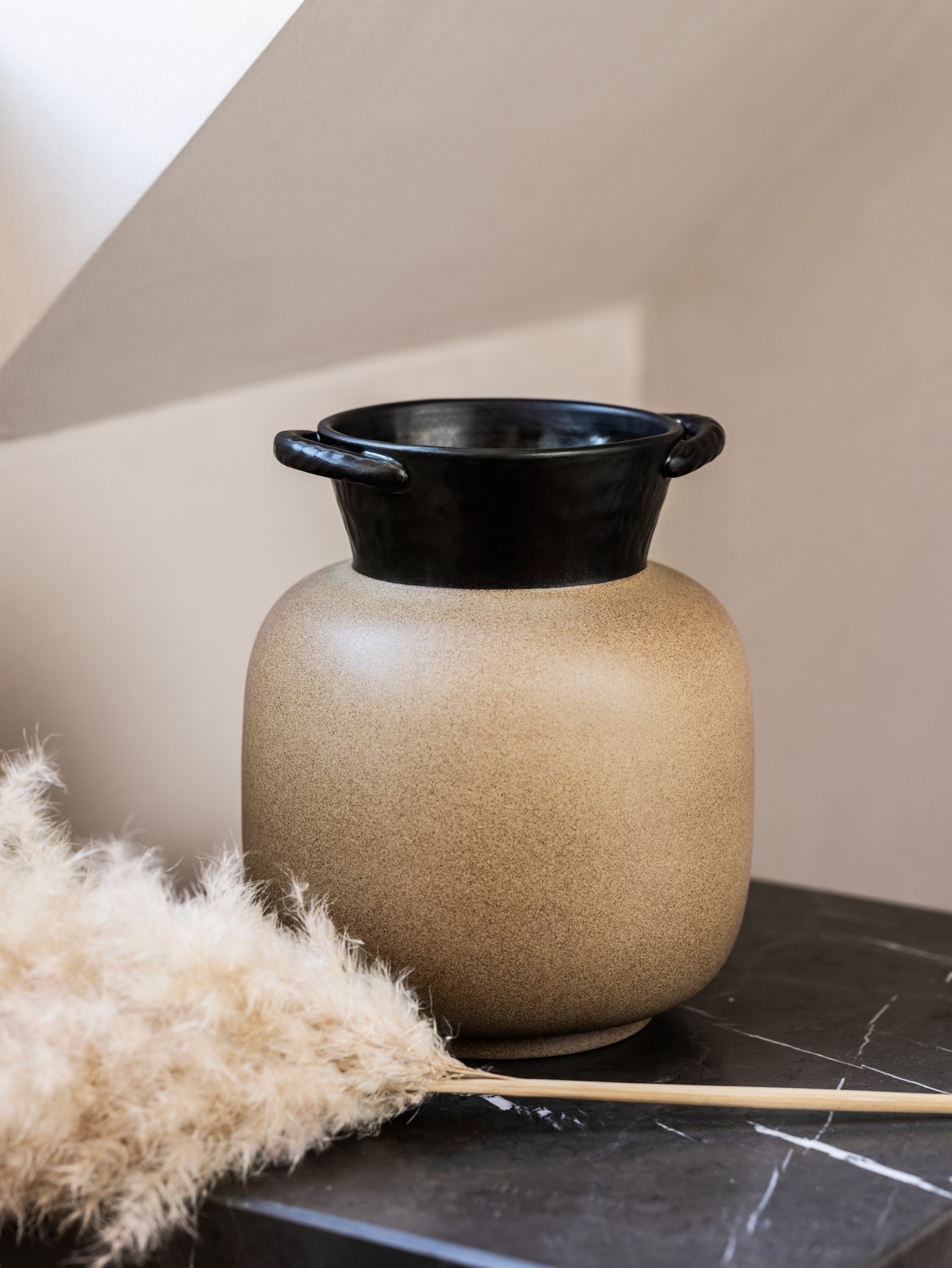 A handmade ceramic vase with two handles, placed on a marble surface against a light background.