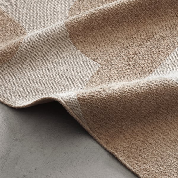 A lamp of unique futuristic design on three short legs, covered in red fabric, on a wooden table top in a darkened room.