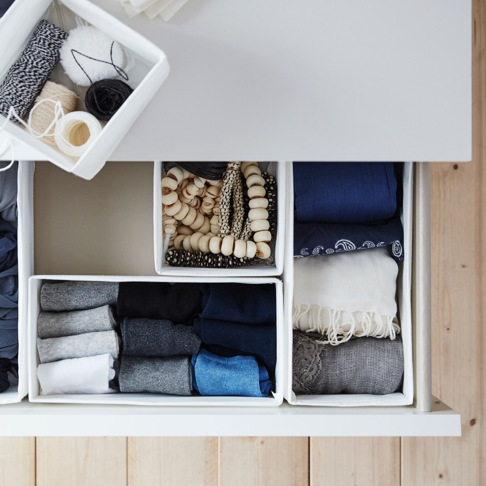 Five white SKUBB boxes of clothes accessories, four in the open top drawer of a white MALM chest of drawers, one on top.