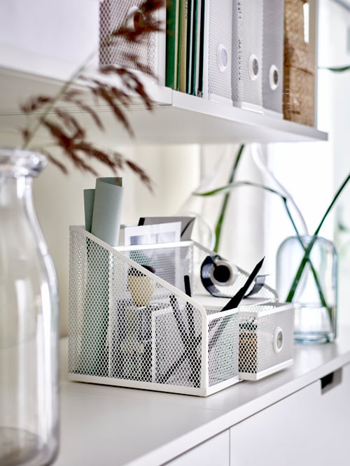 Two shelves with a white DRÖNJÖNS mesh desk organizer holding small office supplies, glass vases and DRÖNJÖNS magazine files.