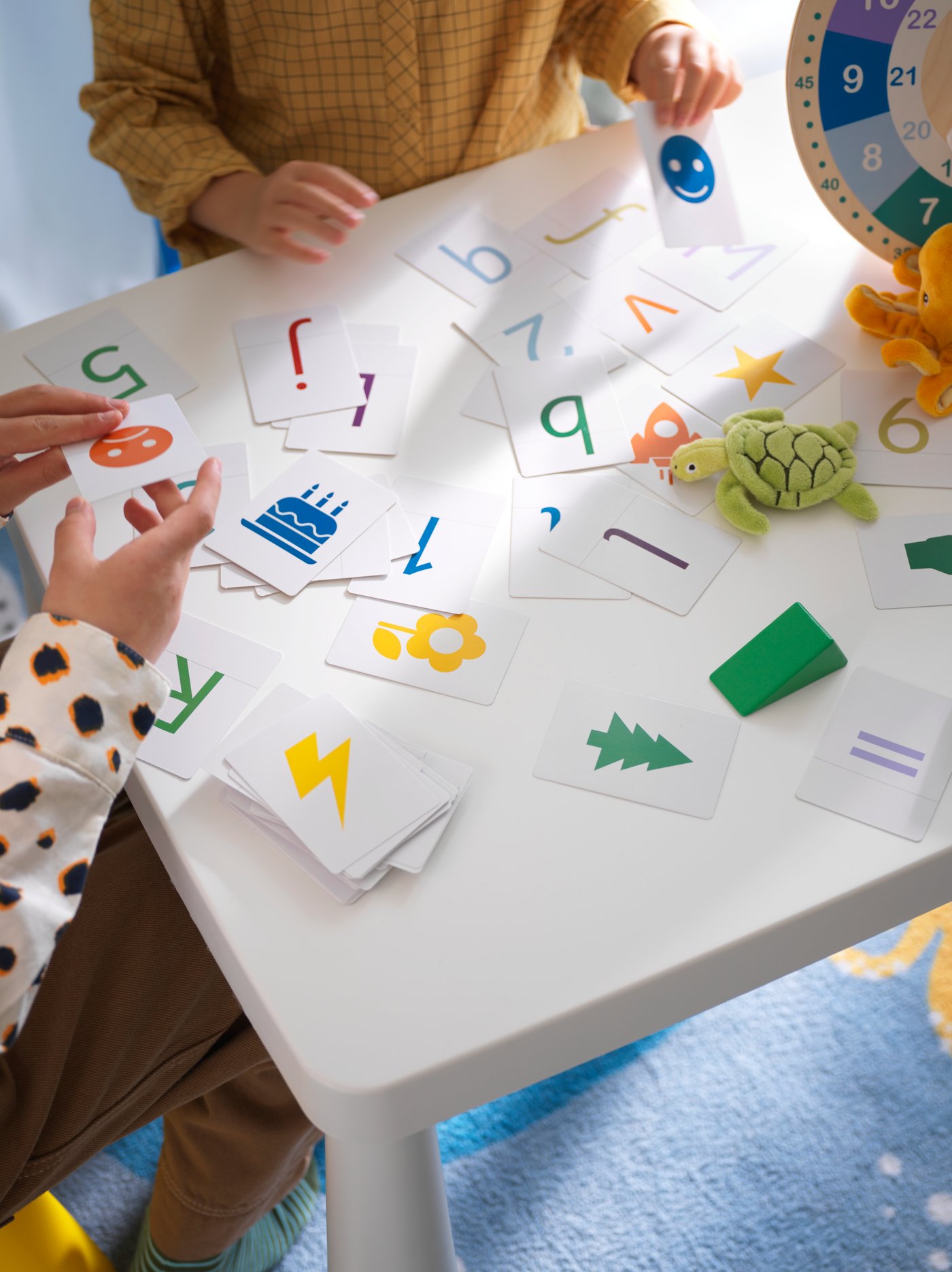 Close up shot from above of table where two children are playing with UNDERHÅLLA cards on a white table.