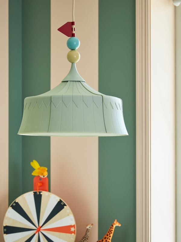 A children’s room where a TROLLBO pendant lamp with a decorated cord hangs above toy animals and a wheel of fortune.